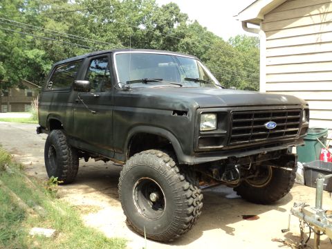 1986 Ford Bronco - This lifted Ford Bronco is parked in a driveway with trees in the background.