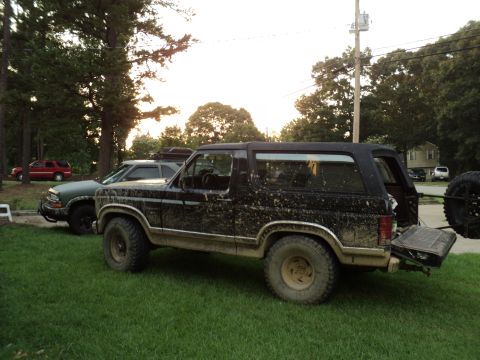 1986 Ford Bronco - This muddy 1986 Ford Bronco is parked on a grassy lawn with another SUV nearby.