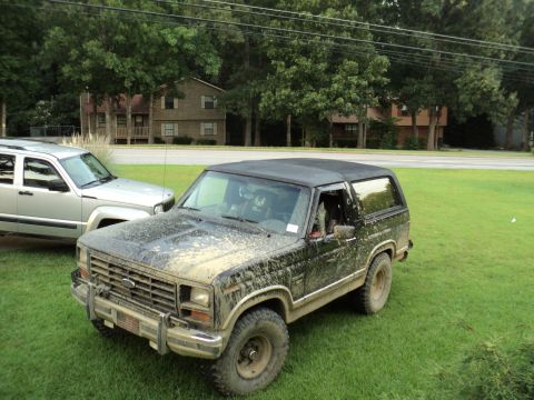 1986 Ford Bronco - A muddy 1986 Ford Bronco sits on a grassy lawn beside a silver SUV.