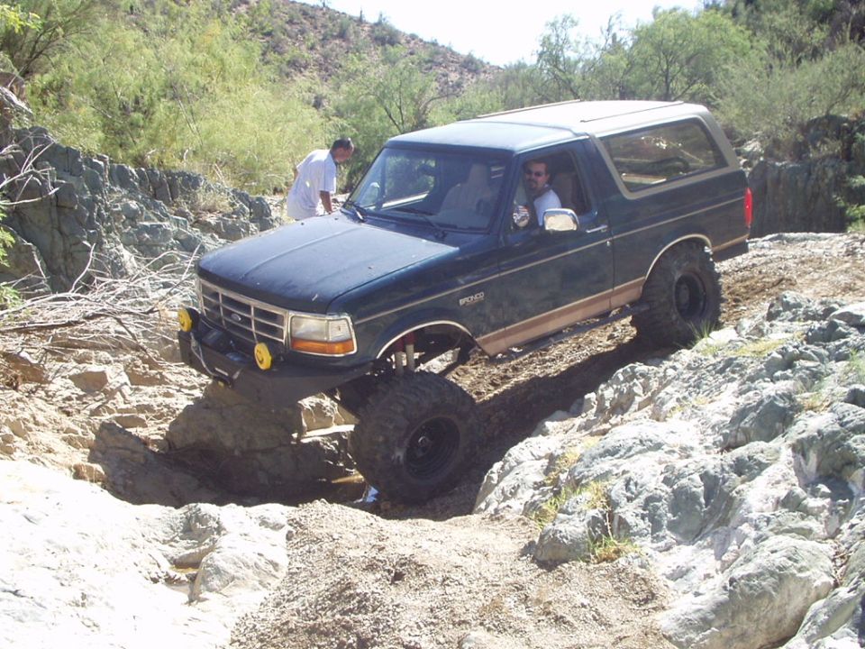 Green and tan lifted Ford Bronco crawling over desert rocks with a spotter