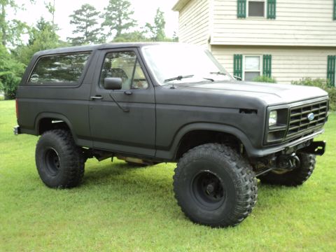 1986 Ford Bronco - This modified Ford Bronco sits on a grassy lawn, its off-road tires and dark matte paint job.