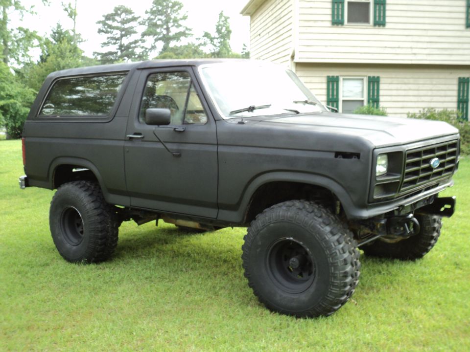 Black Ford Bronco with lifted suspension and large tires parked on grass in front of a house