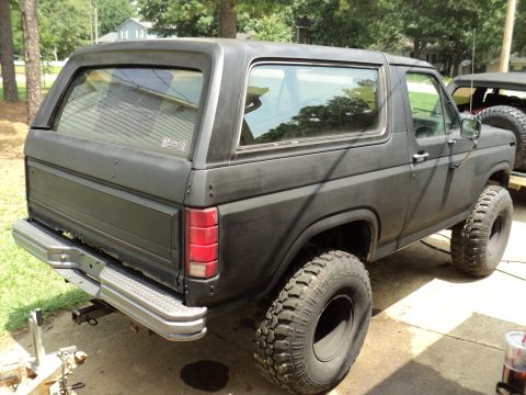 1986 Ford Bronco - This 1986 Ford Bronco is shown from the rear three-quarter view, a matte black finish and aggressive off-road tires.