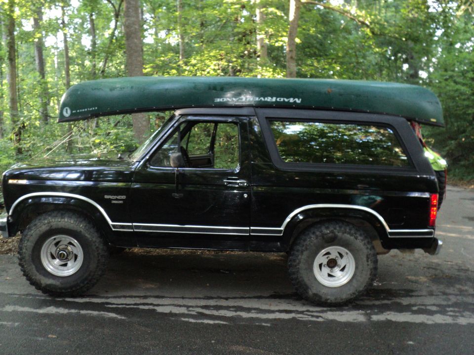 Black 1986 Ford Bronco with green canoe on roof rack