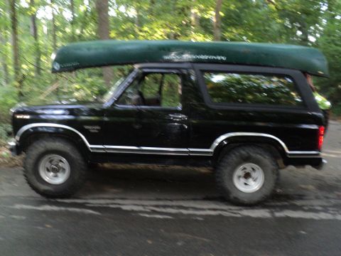 1986 Ford Bronco - A black 1986 Ford Bronco is shown from the side, equipped with a canoe on its roof rack.