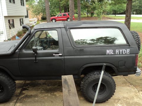 1986 Ford Bronco - Side view of a modified black Ford Bronco, with a red SUV visible in the background.