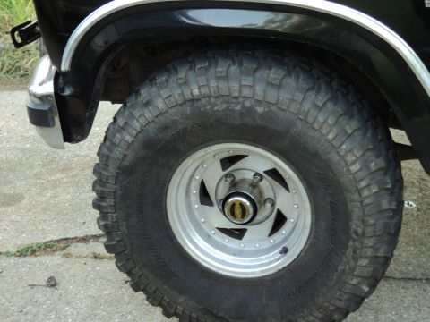 1986 Ford Bronco - The front wheel and fender of a black Ford Bronco are shown, off-road tires and chrome accents.