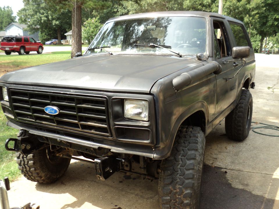 Ford Bronco with large tires and aftermarket bumper. Another red SUV is parked in the background