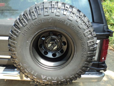 1986 Ford Bronco - Spare tire with Mickey Thompson Baja MTZ tread is mounted on the rear of a black SUV.