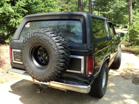 1986 Ford Bronco - Rear view of a black SUV with a spare tire mounted on the tailgate, parked outdoors.