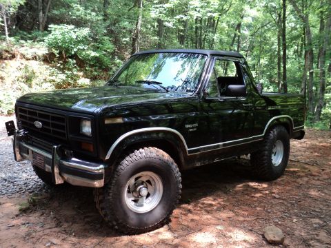 1986 Ford Bronco - This 1986 Ford Bronco is parked on a dirt road surrounded by trees.