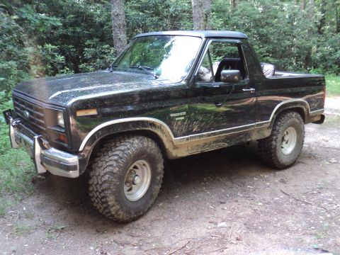 1986 Ford Bronco - This black Ford Bronco is shown on a wooded trail with mud splattered on its body.
