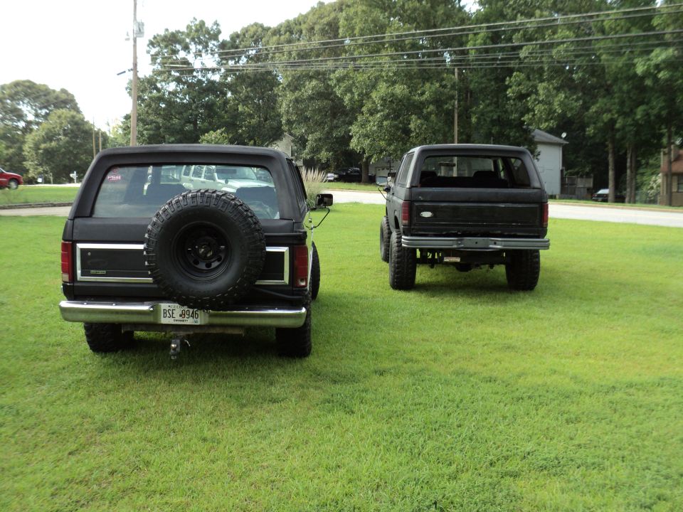 Rear view of two black 1986 Ford Broncos, one with a spare tire mounted on the back