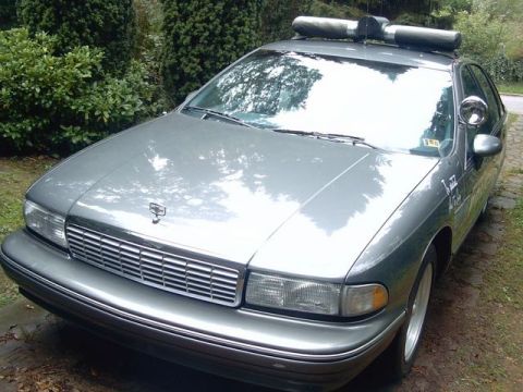1991 Ford LTD Crown Victoria - This police car is parked outside with trees in the background. It has a light bar on the roof.