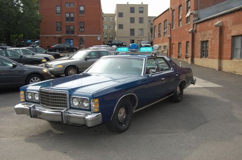 1991 Ford LTD Crown Victoria - This police car, likely a 1977 model, is parked among other vehicles.