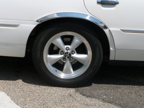 1999 Mercury Grand Marquis - Close-up of a white sedan's rear wheel, chrome fender trim and a five-spoke alloy wheel.