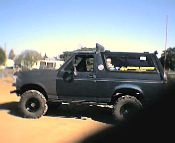 1987 Ford Bronco - This lifted 1987 Ford Bronco features aftermarket wheels and a dark paint scheme, seen from a three-quarter front perspective.