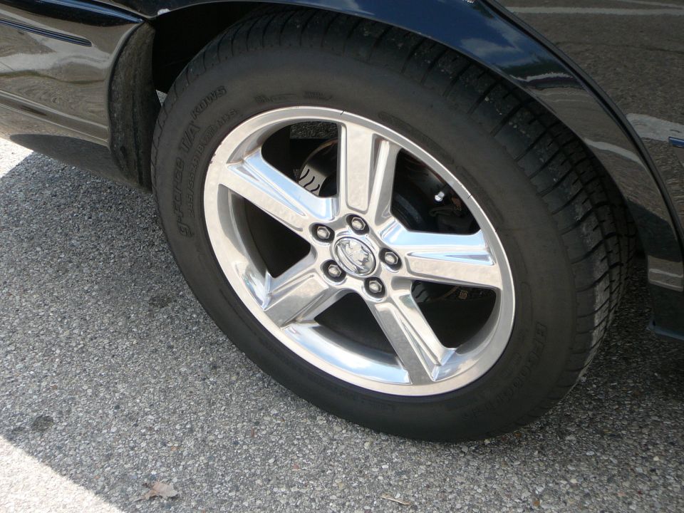 Black car wheel with chrome five-spoke rim and a Mercury emblem. Tire is black