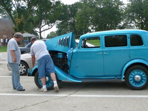 1999 Mercury Grand Marquis - Men inspect a classic blue sedan with its hood open, parked next to a contemporary car.