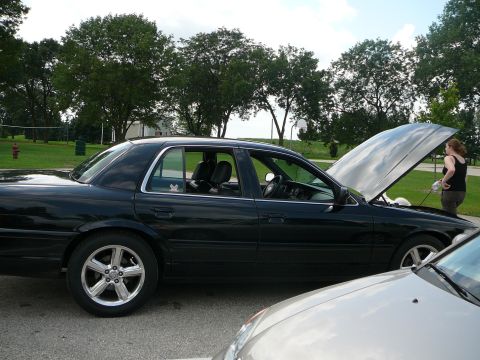 1999 Mercury Grand Marquis - A black sedan has its hood open while a person attends to the engine, with another vehicle partially visible in the foreground.