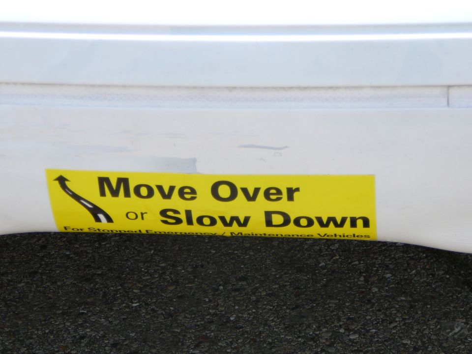 Yellow sticker with black text 'Move Over or Slow Down' and a graphic of a road curving away