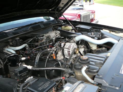 1999 Mercury Grand Marquis - The engine compartment of a vehicle is shown with various components and hoses. Another car is visible in the background.