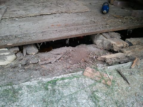 1985 Ford F-150 - A hole in a wooden floor reveals dirt and debris underneath.
