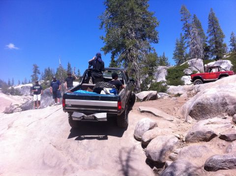 1990 Ford Bronco - A red Ford Bronco navigates a rocky trail with other vehicles and people present.