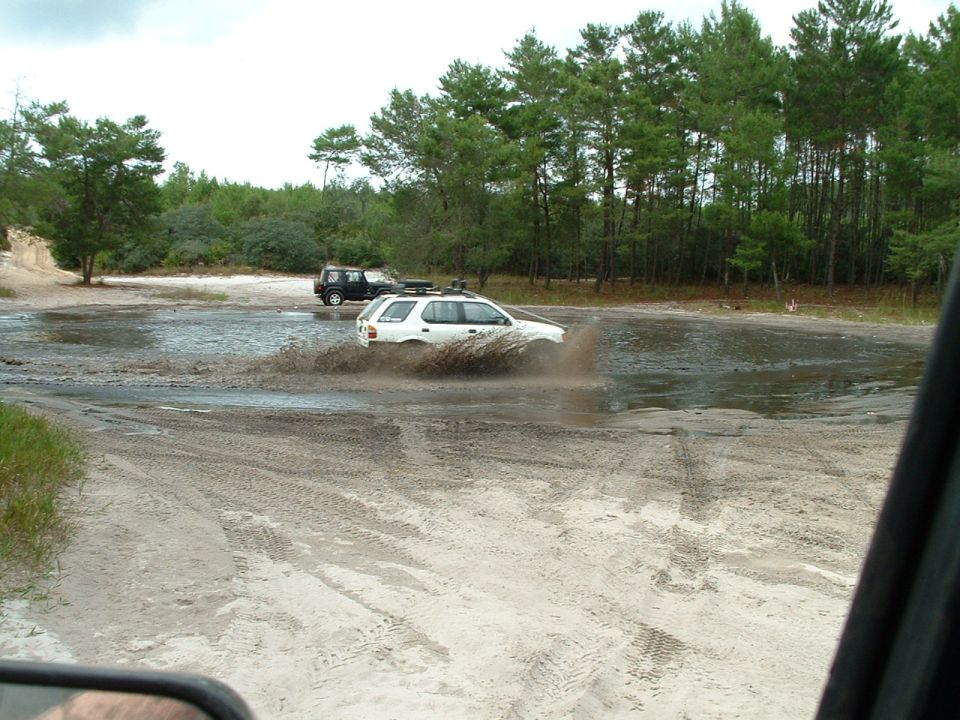 White SUV splashing through mud, black SUV in background