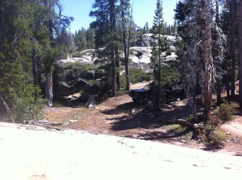 1990 Ford Bronco - A dark-colored SUV is parked on a dirt path surrounded by trees and rocks.