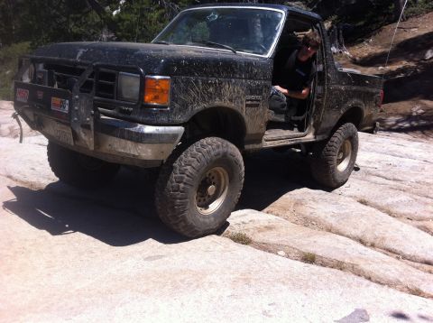 1990 Ford Bronco - A black Ford Bronco navigates a rocky trail, its driver visible through the open door.