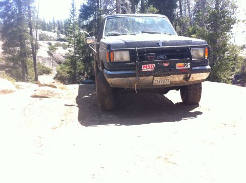 1990 Ford Bronco - 1990 Ford Bronco parked off-road in a wooded, rocky area.