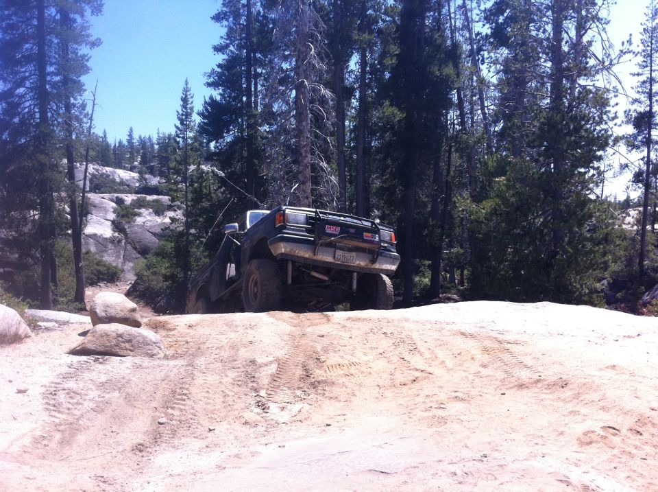 Dark green 1987 Ford Bronco off-roading on a dirt hill with trees and rocks