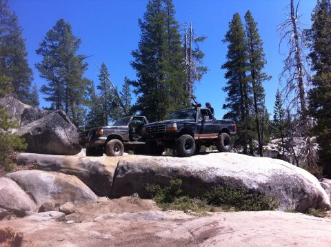 1990 Ford Bronco - Two trucks navigate rocky terrain under a clear blue sky.
