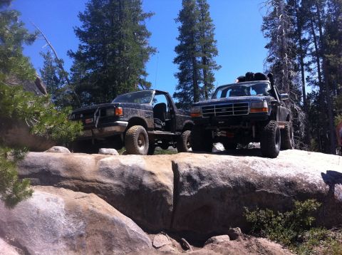 1990 Ford Bronco - Two Ford trucks are parked on large rocks in a wooded, sunny area.