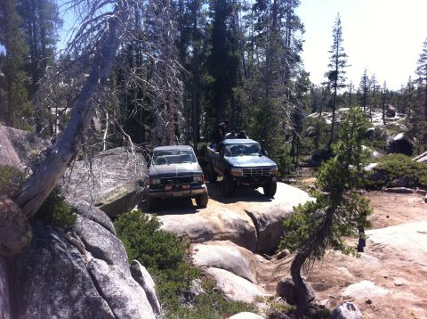 1990 Ford Bronco - Two trucks are parked on large rocks in a forest setting during an off-road excursion.