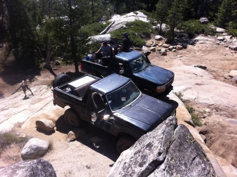 1990 Ford Bronco - Two trucks navigate a rocky, off-road trail with several people riding in one of the vehicles.