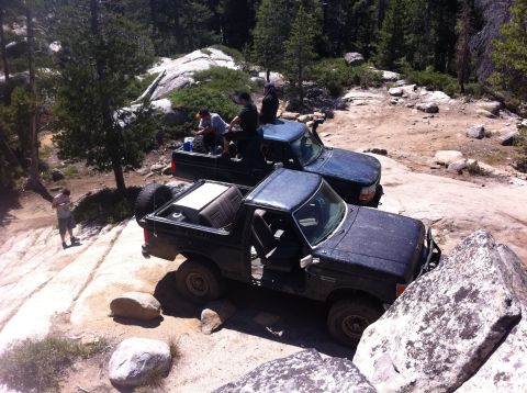1990 Ford Bronco - Two off-road vehicles navigate a rocky trail with people standing around.