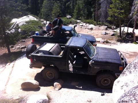 1990 Ford Bronco - Two off-road vehicles, a Bronco and a pickup, navigate a rocky trail in a wooded area.
