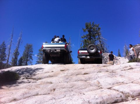 1990 Ford Bronco - Two trucks navigate a steep, rocky incline under a clear blue sky.