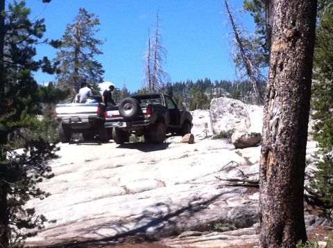 1990 Ford Bronco - Two trucks navigate a challenging rocky path in a wooded, mountainous area.