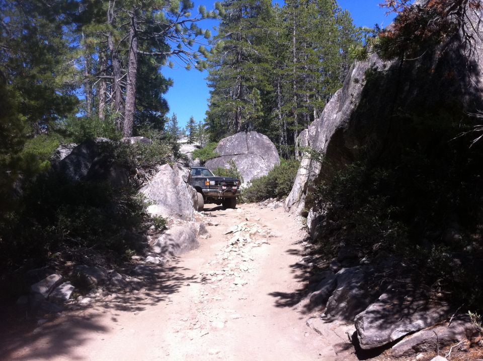 Dark SUV on a rocky, off-road path with large boulders and pine trees