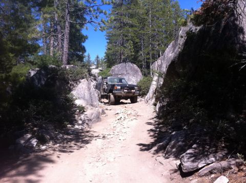 1990 Ford Bronco - A black 1990 Ford Bronco navigates a challenging rocky trail surrounded by trees and boulders.