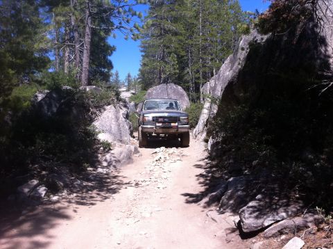1990 Ford Bronco - Ford F-Series truck driving on a rough, off-road trail through a wooded, rocky area.