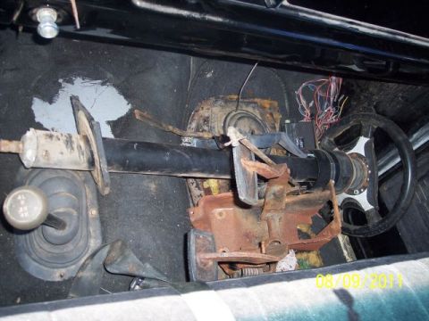 1978 Ford Bronco - The interior of a vehicle is shown, focusing on the steering column, dashboard components, and a four-wheel-drive shifter. Rust is visible…