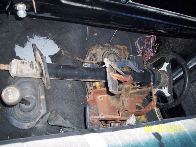 Interior view of a vehicle's steering column, dashboard, and gear shifter with visible rust