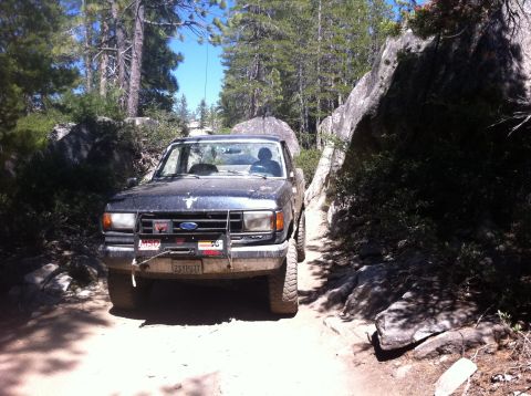 1990 Ford Bronco - Ford Bronco on a tight trail, navigating around large rocks and trees.