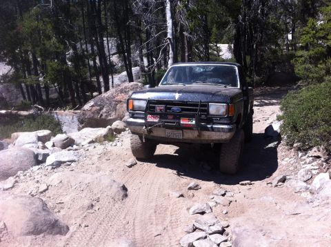 1990 Ford Bronco - A black Ford Bronco navigates a challenging, rocky off-road trail.