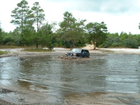 1995 Ford Bronco - A dark 1995 Ford Bronco navigates through a muddy water obstacle.