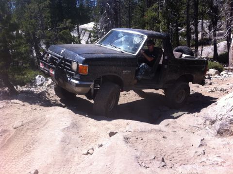 1990 Ford Bronco - A driver navigates a rough, rocky trail in a black Ford Bronco.